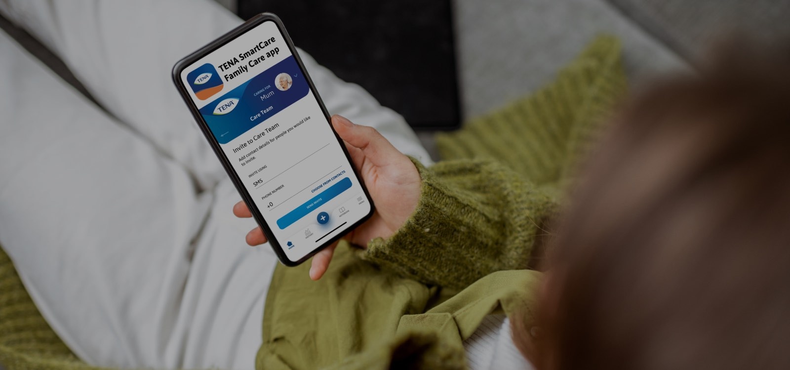 Over the should of a woman using the TENA SmartCare Family Care app on her phone.