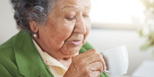 An elderly woman drinks coffee. 