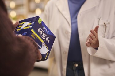 A pharmacist talks with a male customer who is holding a pack of TENA incontinence products for men.