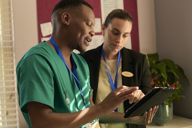 A male professional caregiver and a female TENA representative look at a tablet and have a discussion together in a care facility