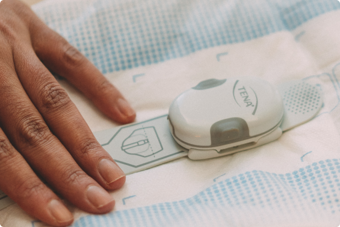 Une image montrant le transmetteur de TENA SmartCare Change Indicator qui collecte des informations sur les taux de saturation et les envoie aux smartphones des soignants.