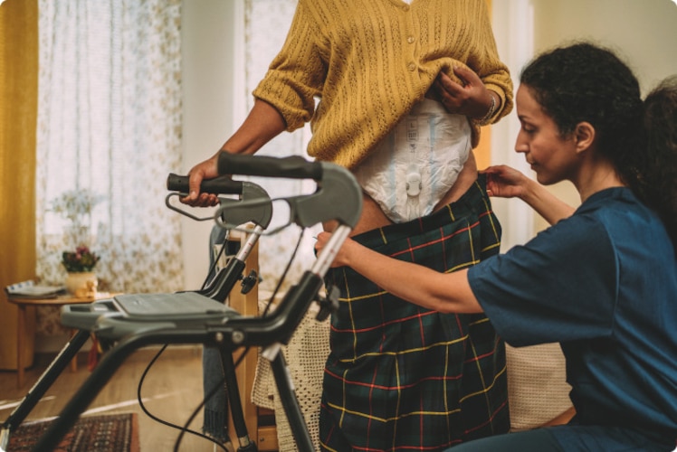 Bewohnerin eines Pflegeheims, die den TENA SmartCare Wechselindikator™ trägt, erhält Unterstützung beim Ankleiden durch eine professionelle Pflegekraft.