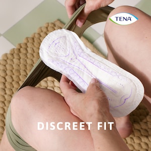 Person sitting down and holding the TENA Discreet Ultra pad in hand, ready to insert it into their underwear