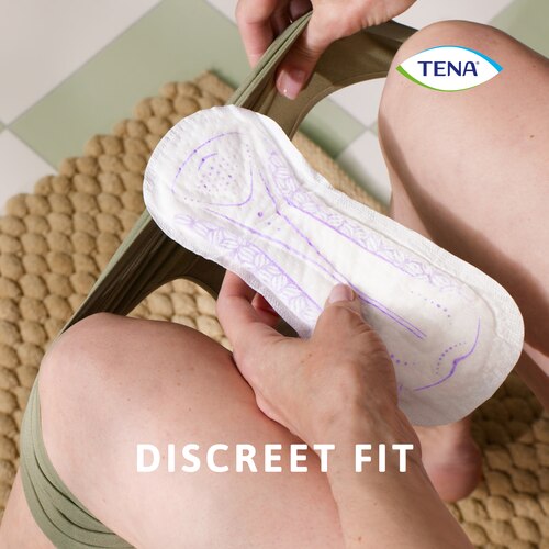 Sedeča ženska, ki v roki drži vložek TENA Lady Slim Ultra Mini, da ga namesti v spodnje hlačke