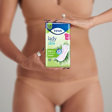 Biała kobieta w beżowej bieliźnie, z pierścionkami na palcach, trzymająca opakowanie TENA Lady Mini przed sobą. Biała kobieta w beżowej bieliźnie, z pierścionkami na palcach, trzymająca opakowanie TENA Lady Mini przed sobą.