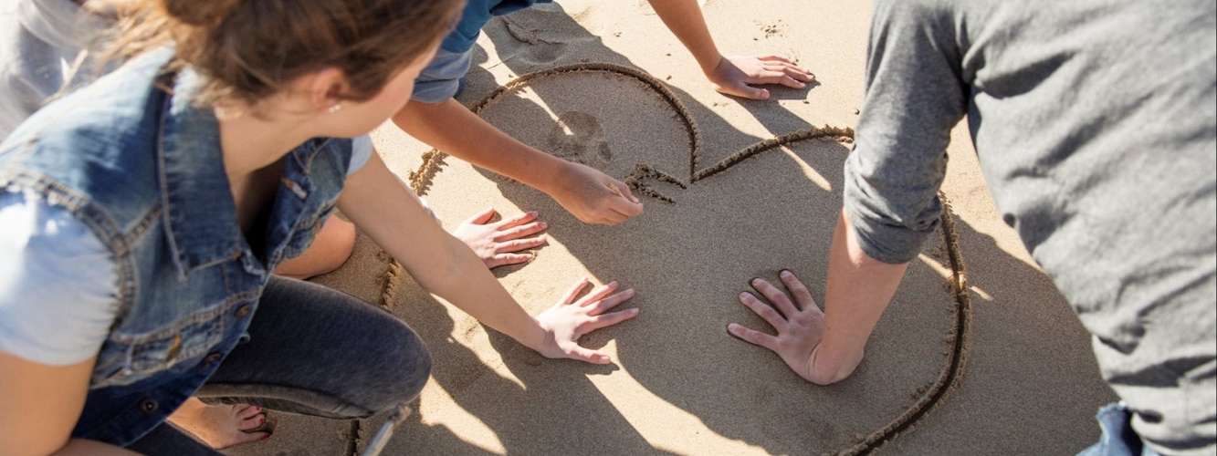 Personer som ritar ett hjärta i sanden. 
