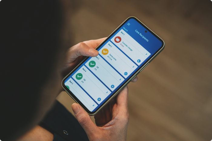 Une soignante professionnelle examine les notifications et le statut de saturation des produits absorbants des résidents sur son smartphone.