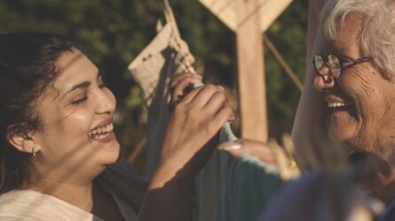 Two women laugh while having a conversation over a washing line.