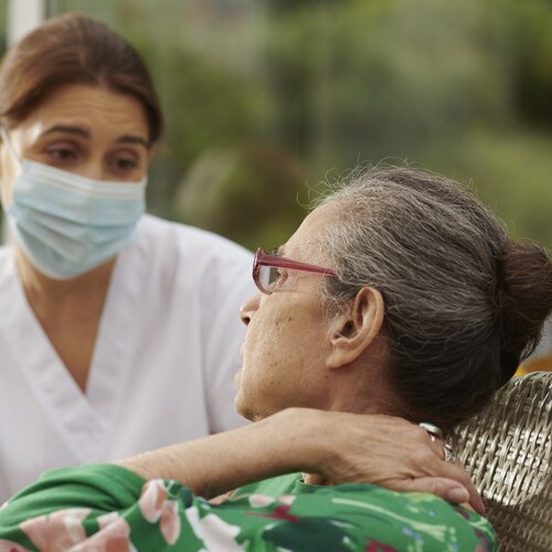 Pflegekraft tröstet eine ältere Frau im Freien.