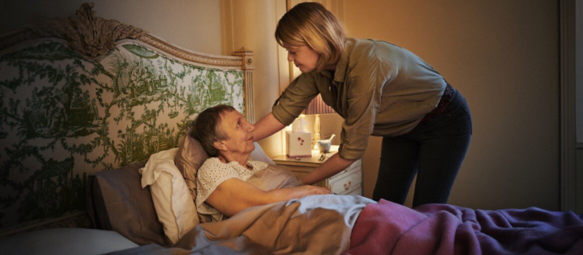 Kobieta pomaga starszej osobie leżącej w łóżku