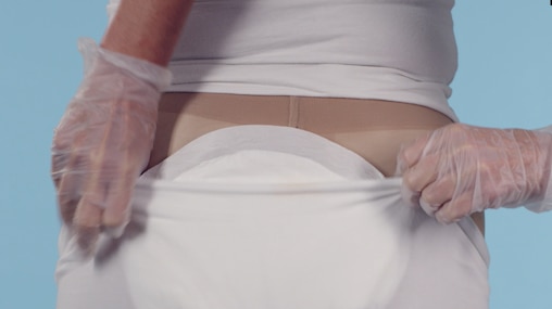 Imagem fixa de um vídeo com cuidador a ajudar a colocar fraldas TENA num ente querido em posição levantada.