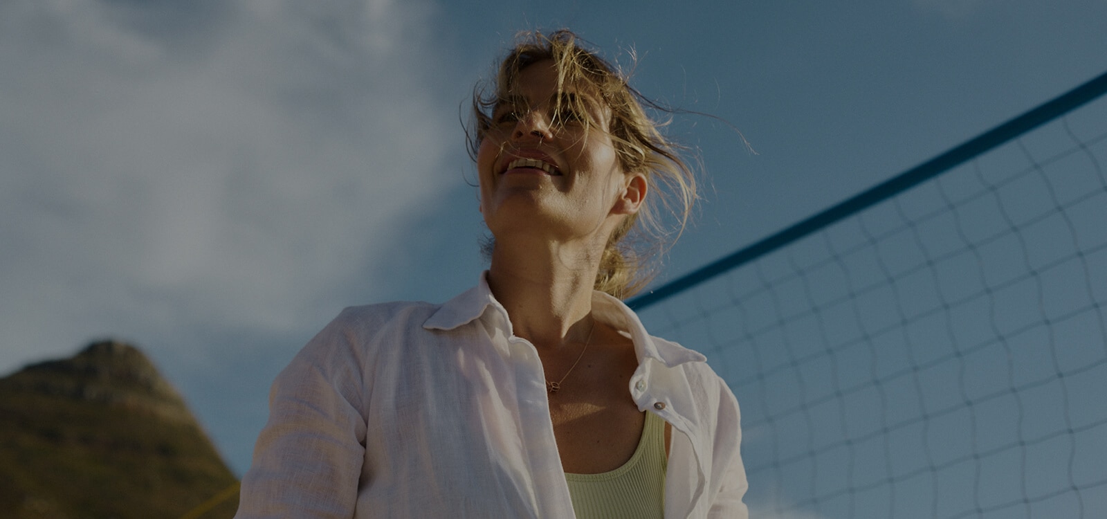 Mulher na praia a sorrir em frente a uma rede de voleibol