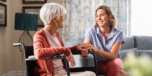 Ältere Frau umarmt jüngere Frau im Sitzen – hilfreiche Informationen über die Durchführung von Pflegeaufgaben