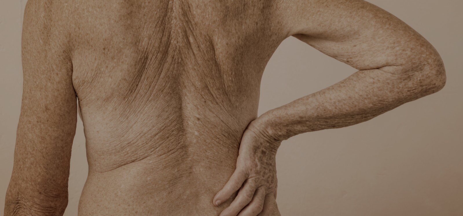 An older person with their back to camera and exposed skin, resting hand on hip