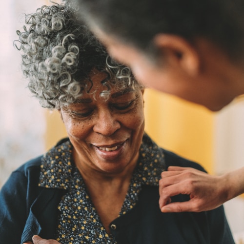 A close up of a female professional caregiver with her hand on a female resident's shoulder