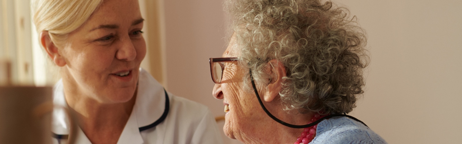 A smiling female professional caregiver talks with an elderly female resident in a nursing home environment