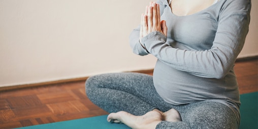 Een zwangere vrouw die met gekruiste benen in een yogahouding zit