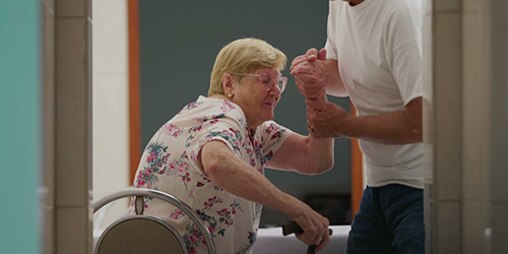 Caregiver con problemi alla schiena che aiuta una donna a sedersi su una sedia a rotelle
