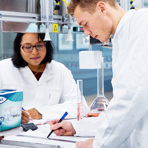 Zwei Wissenschaftler in Laborkitteln arbeiten gemeinsam an Forschung mit sichtbarem TENA-Produkt im Laborumfeld.