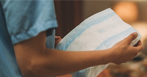 A close-up image of a professional caregiver holding a TENA absorbent product in a nursing home environment