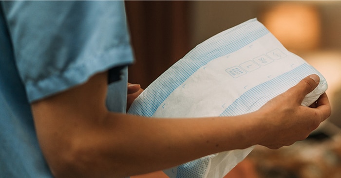 A close-up image of a professional caregiver holding a TENA absorbent product in a nursing home environment