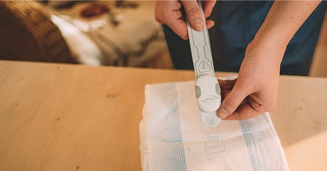 A close-up image of a professional caregiver attaching a TENA SmartCare Change Indicator Sensor Strip to a TENA absorbent product 