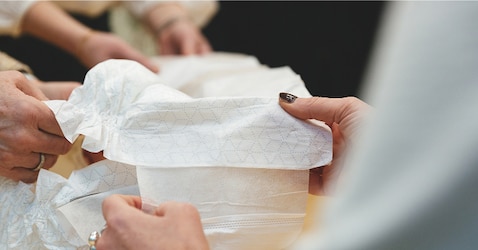 A close-up image of two pairs of hands holding a TENA absorbent product 