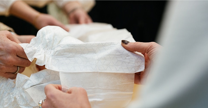 A close-up image of two pairs of hands holding a TENA absorbent product 