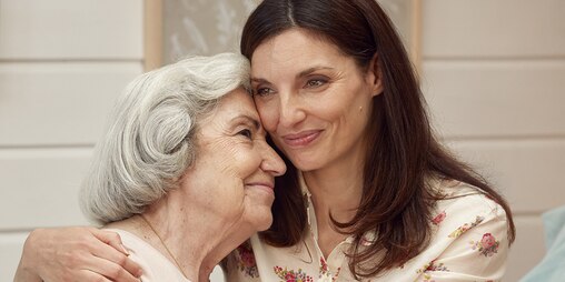 Jüngere Frau umarmt ältere Frau – finden Sie heraus, warum TENA Produkte für Ihren Angehörigen am besten sind.