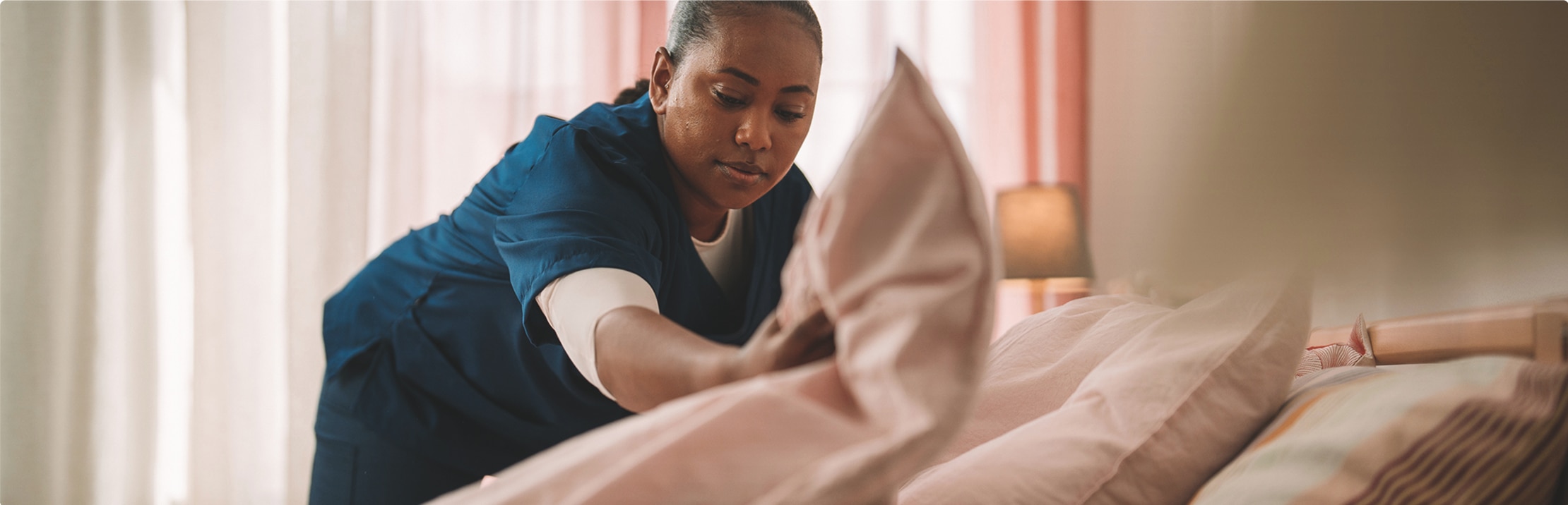 A professional caregiver makes a resident’s bed in a comfortable nursing home environment. 