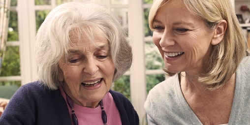 Una donna anziana e una più giovane ridono insieme – Ricerca di organizzazioni di supporto per l’attività assistenziale