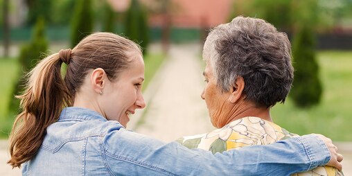 Ältere Frau sitzt mit jüngerer Frau draußen – planen Sie Ihre Pflegeaufgaben