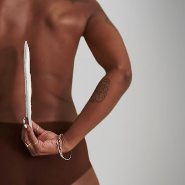 A picture of a black woman holding a TENA pad behind her back, illustrating how thin it is.