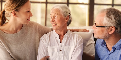 Älteres Paar sitzt mit junger Frau zusammen – wie Sie Ihren Angehörigen pflegen, ohne Ihren Körper dabei zu überanstrengen