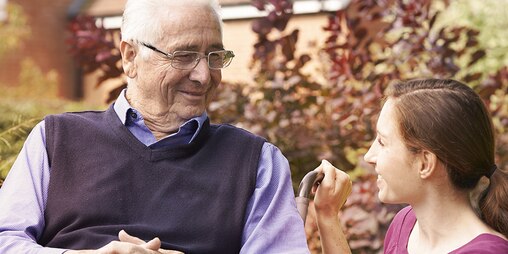 Idős férfi a szabadban ül egy fiatal nő társaságában – Olvasson bővebben más ápolók tapasztalatairól