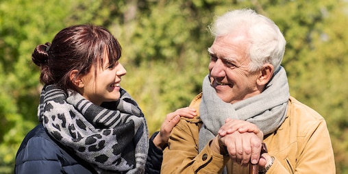 Un uomo anziano seduto all’aperto con una giovane donna – Sostegno finanziario per i caregiver