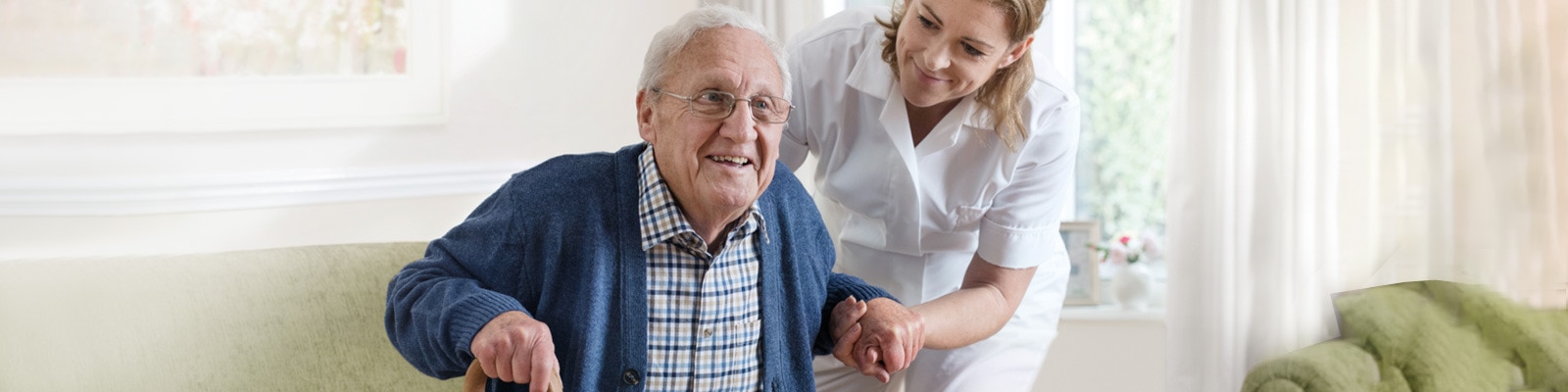 Una caregiver in uniforme bianca aiuta un uomo anziano a sedersi 