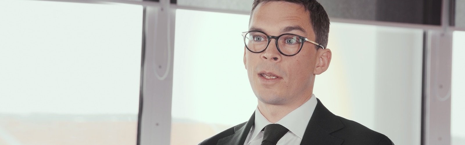 Vêtu d’un costume sombre et assis dans un bureau, Axel Nordberg s’adresse à un intervieweur hors champ. 