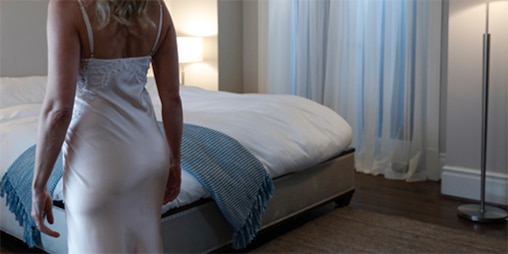 A woman in attractive nightwear in front of her bed