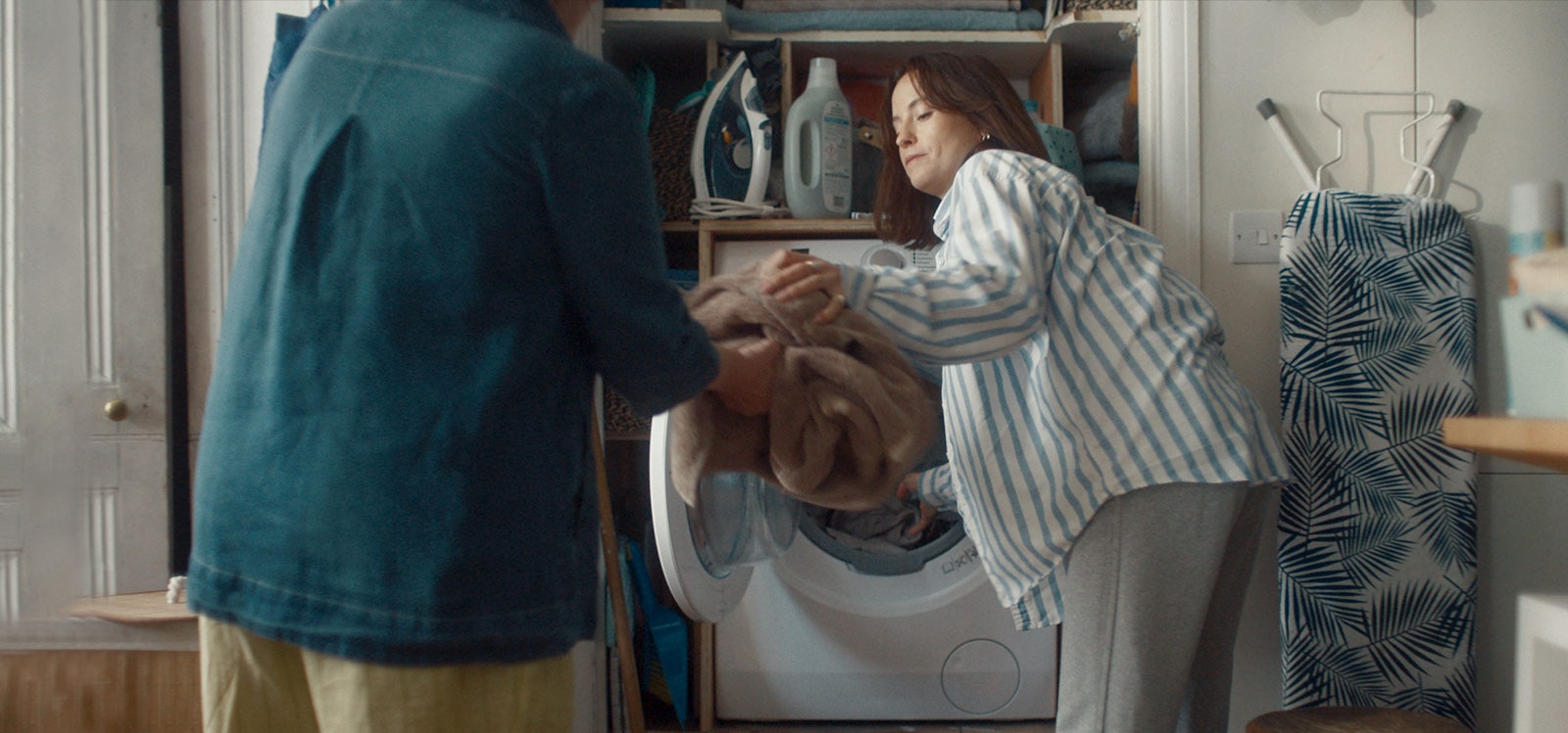 Moteris išima iš skalbimo mašinos skalbinius ir paduoda juos mamai.