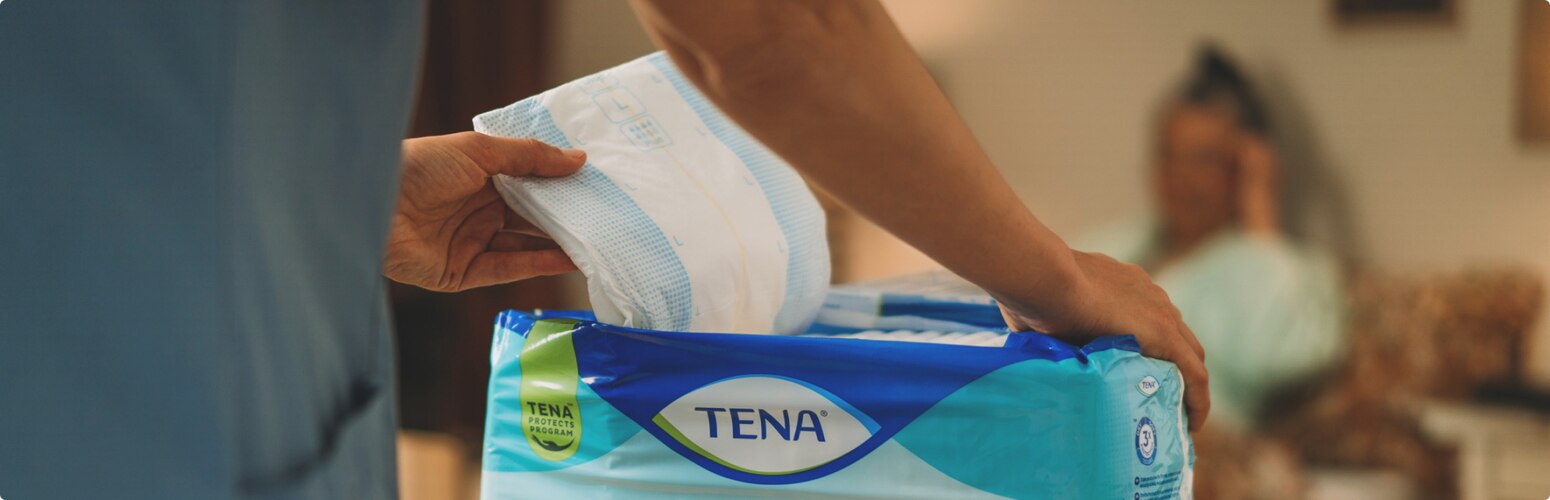 A professional caregiver removes a TENA absorbent product from its packaging.