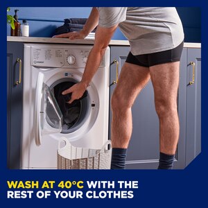 A man wearing the TENA Men washable underwear leaning down to throw another pair of used underwear into a washing machine. There is a caption at the bottom saying "wash at 40 degrees Celsius with the rest of your clothes".