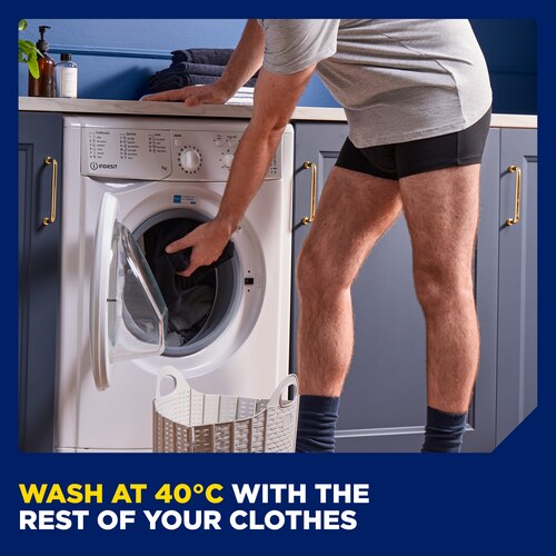 A man wearing the TENA Men washable underwear leaning down to throw another pair of used underwear into a washing machine. There is a caption at the bottom saying "wash at 40 degrees Celsius with the rest of your clothes".