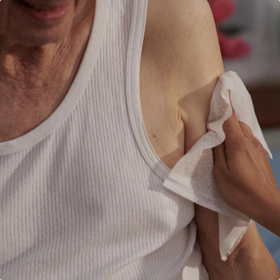A close-up showing the hand of a professional caregiver as they gently clean the skin on the upper arm of an elderly nursing home resident  