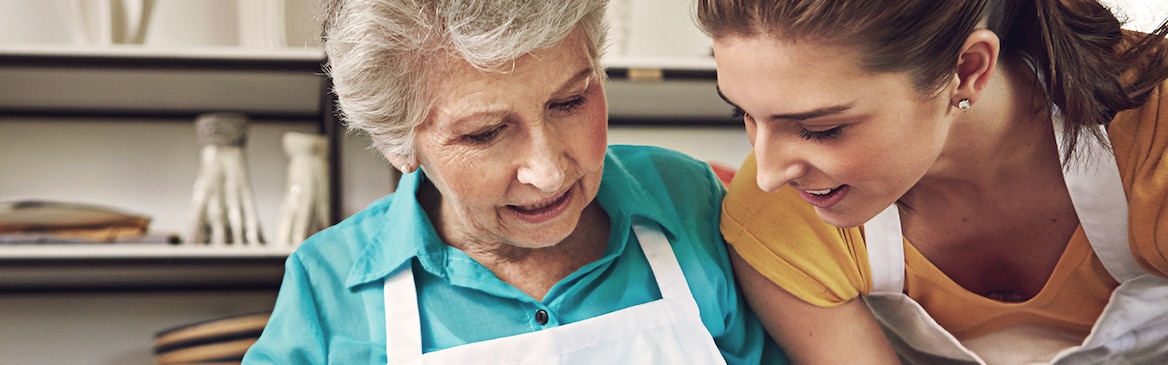 Idős nő süteményt süt egy fiatal nővel közösen – Az ápolással kapcsolatos leggyakoribb kérdések és a rájuk adott válaszok