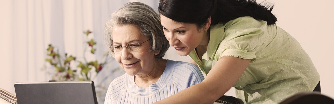 Starejša gospa in mlajša ženska uporabljata računalnik – kako Alzheimerjeva bolezen vpliva na vaše bližnje