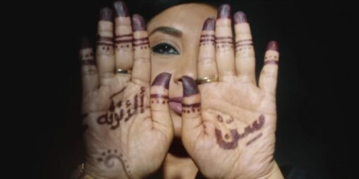 Woman holding up her hands towards the camera, her hands have henna drawings and text on them. 