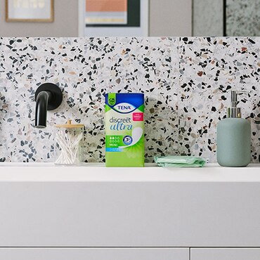 Paquete de TENA Discreet Mini sobre la encimera de un baño