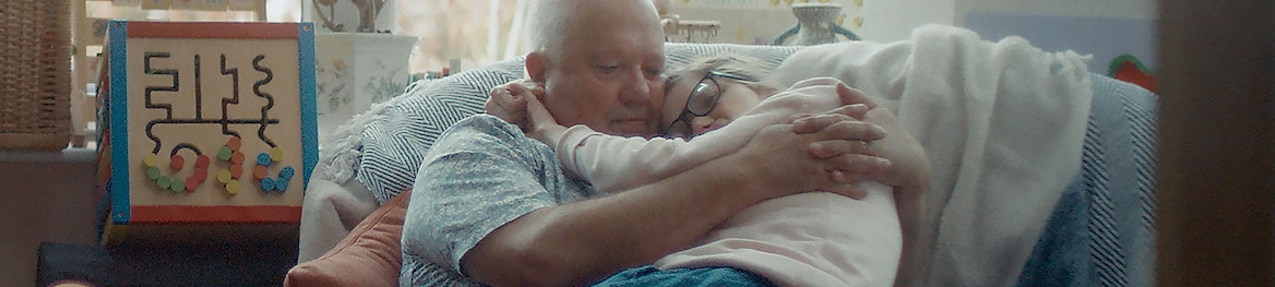 Un hombre de mediana edad abraza a su hija adolescente en el sofá.