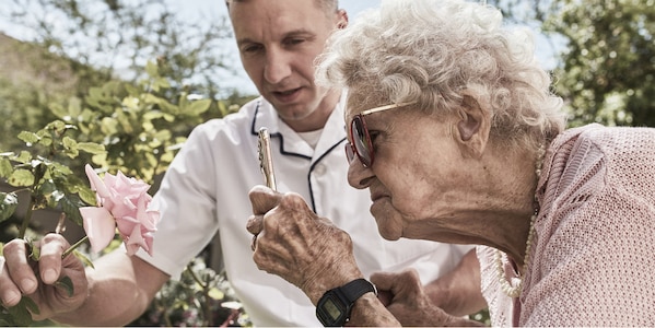Una signora anziana che osserva una rosa insieme a un infermiere